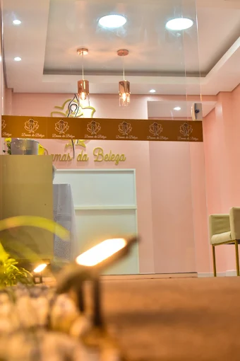 Recepção da Damas da Beleza: parede rosa-quartzo, logo dourada em relevo e pendentes de vidro cor de cobre acesos.