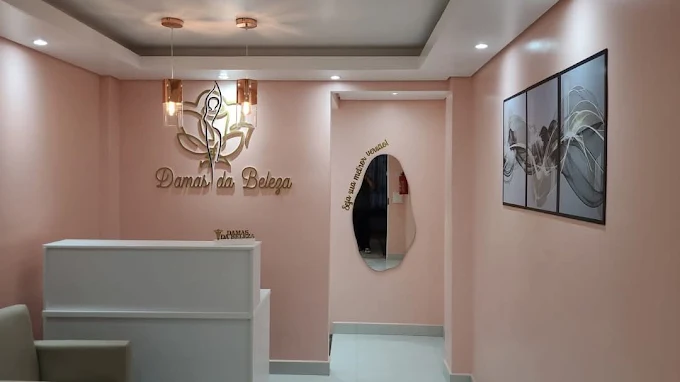 Recepção vista de dentro: balcão branco, logo dourada na parede rosa e o espelho de formato orgânico com a frase em dourado.